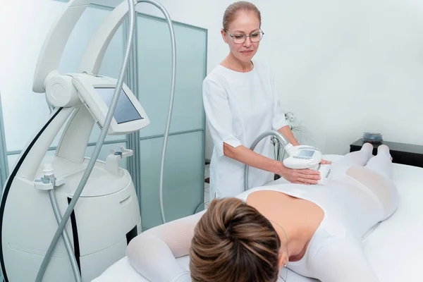 Mujer en traje blanco especial recibiendo masaje anti celulitis en un salón de spa. GLP, y tratamiento de contorno corporal en la clínica. — Foto de Stock