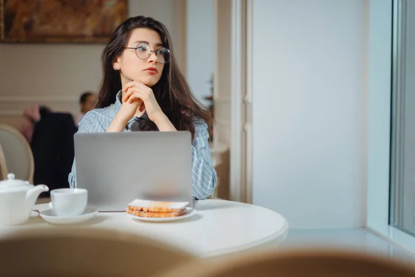 Uzak mesafe işi için dizüstü bilgisayarı kullanan genç bir kadının portresi. Modern kahve dükkanının içinde otururken, akıllı bir kadın sabah kahvaltının içinde internet-kitap üzerinde çalışıyor. — Stok fotoğraf