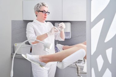 Şırıngalı jinekolog, jinekoloji koltuğundaki hastaya iğne yapıyor.