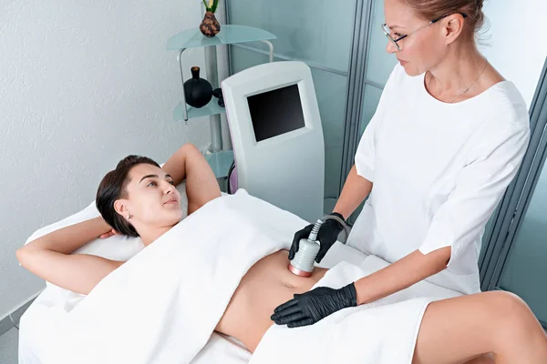 Beautiful woman having cavitation, procedure removing cellulite on legs and belly at beauty clinic
