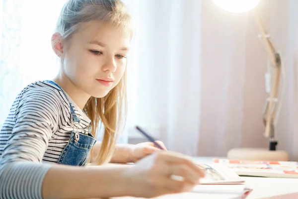 Teenager lernt und macht ihre Hausaufgaben, während sie Stift hält und in ihr Notizbuch schreibt — Stockfoto