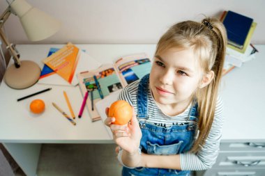 Genç kız masanın yanında duruyor ve ödevlerini yapmaya ara veriyor.