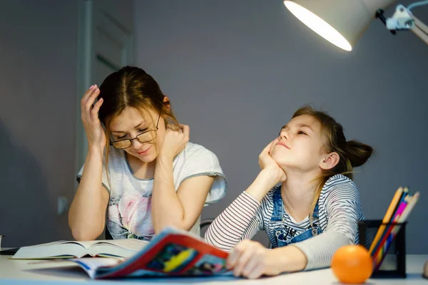 Mother helping her tired daughter with homework at home. — Stock Photo, Image