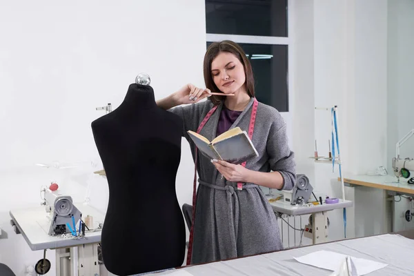 Brunette seamstress measuring black dummy in workshop, tailor studio work — Stock Photo, Image