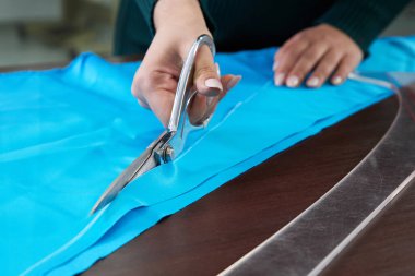 Terzi, atölyede mavi kumaş kesiyor.