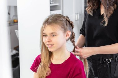 Hair stylist weaves braid to preteen girl in beauty salon