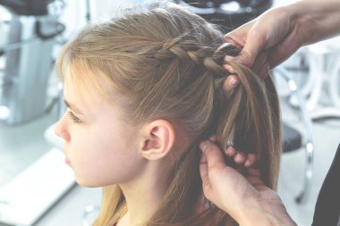 Hair stylist weaves braid to preteen girl in beauty salon