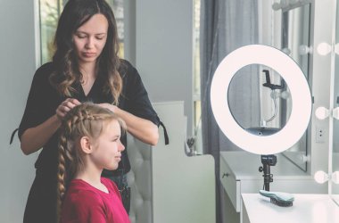 Hair stylist weaves braid to preteen girl in beauty salon