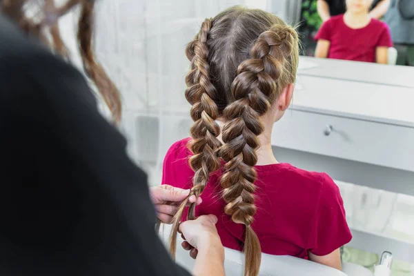 Cabeleireiro tece uma trança para uma menina loira pré-adolescente em um salão de beleza e cabelo — Fotografia de Stock