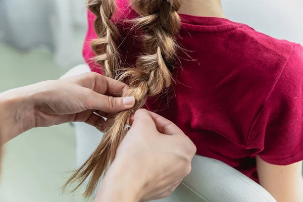 Hairdresser weaves a braid to a preteen blond girl in a beauty and hair salon — 스톡 사진