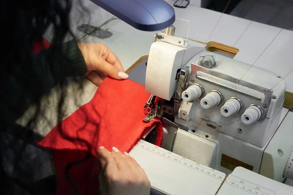 Молодой портной с помощью профессиональной швейной машинки оверлок в мастерской. Оборудование для кромки, зашивания или шитья одежды в магазине портных — стоковое фото