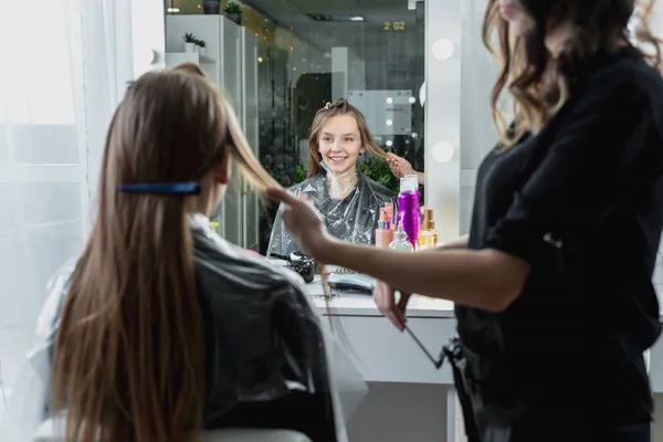Hairdresser brushing long blonde hair with brush in beauty salon