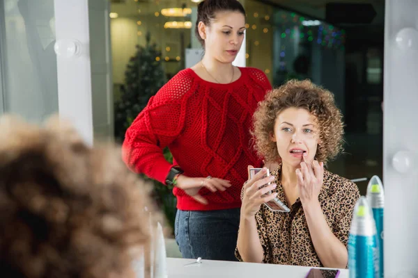 Mujer joven haciendo maquillaje en salón de belleza delante de un espejo mirando su reflejo — Foto de Stock