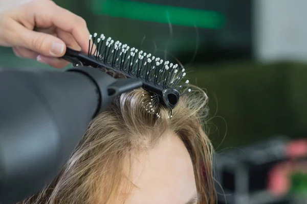 Close up de cabeleireiros mãos secando longos cabelos loiros com secador de cabelo e escova redonda — Fotografia de Stock