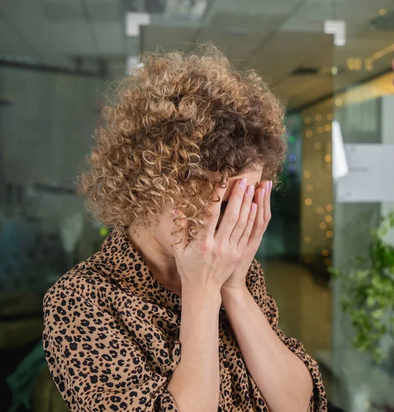 Ofiste ağlarken yüzünü elleriyle kapatan, üzgün yüzlü, kıvırcık, genç bir kadın. Depresyon kavramı — Stok fotoğraf