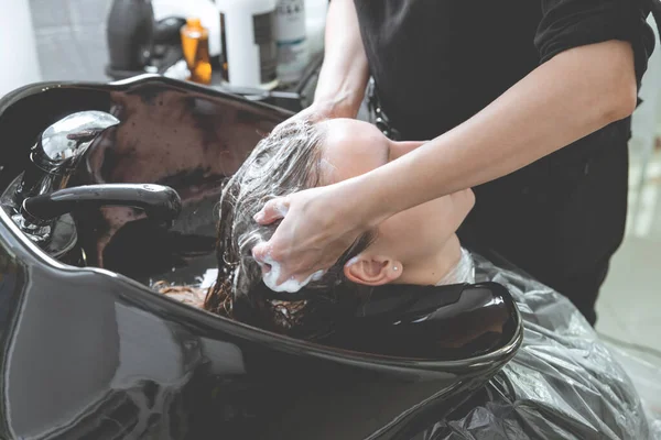 Hair stylist washing hair of yong blonde girl in hair salon before haircut — Stock Photo, Image