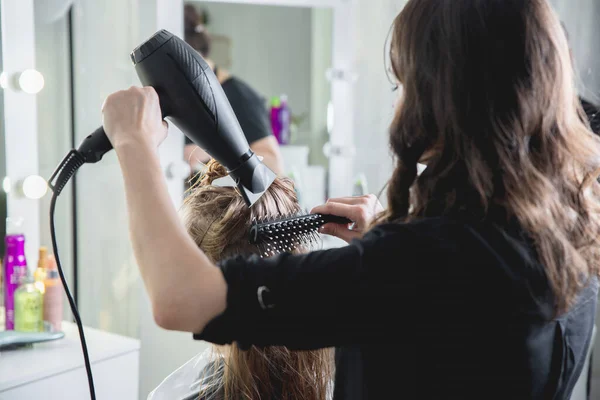 Close up of hairdressers hands drying long blond hair with blow dryer and round brush — Stock Photo, Image