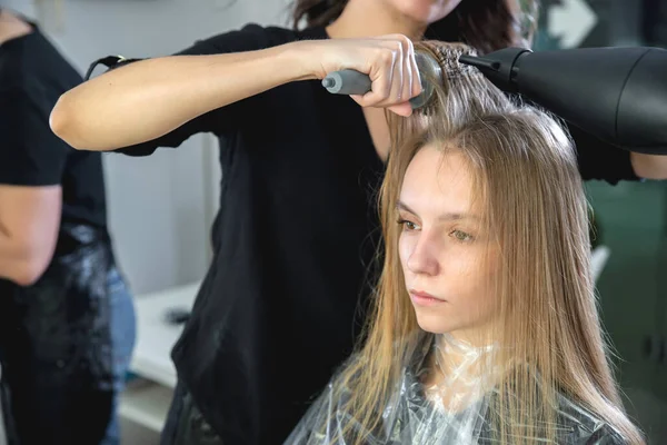 Крупный план рук парикмахеров, высушивающих длинные светлые волосы феном и круглой щеткой — стоковое фото