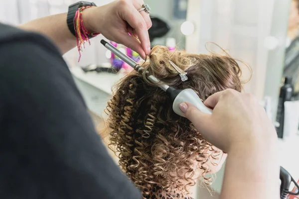 Hairdresser working with beautiful woman in hairdressing salon. Close up view of hand, curling iron and the appliance — Stock Photo, Image