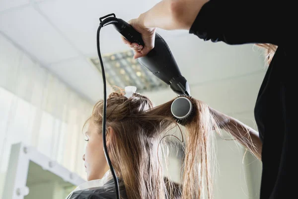 Close up of hairdressers hands drying long blond hair with blow dryer and round brush — Stock Photo, Image