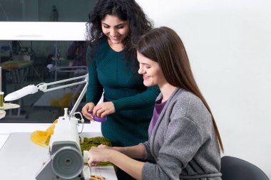Pretty seamstress teaching girl working with sewing machine at sewing class in tailor studio