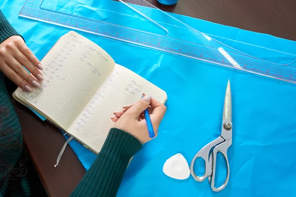 Penjahit menulis langkah-langkah dalam notebook. Si penjahit menciptakan koleksi pakaian. Perancang wanita muda membuat catatan tentang ide-ide di notebook — Stok Foto