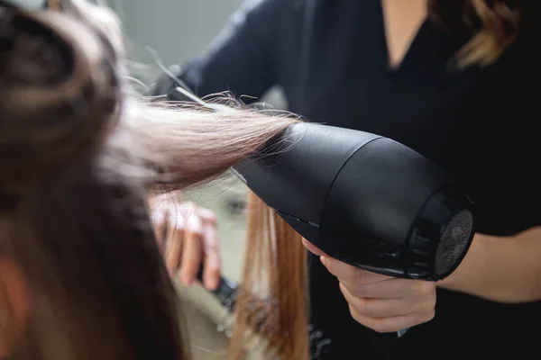 Gros plan de coiffeurs mains séchant de longs cheveux blonds avec sèche-cheveux et brosse ronde — Photo