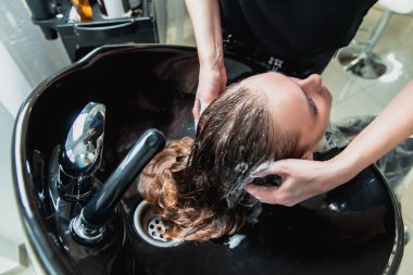 Saç stilisti. Saç tıraşından önce kuaförde sarışın bir kızın saçını yıkıyor.