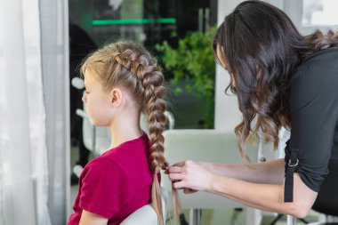 Hair stylist weaves braid to preteen girl in beauty salon