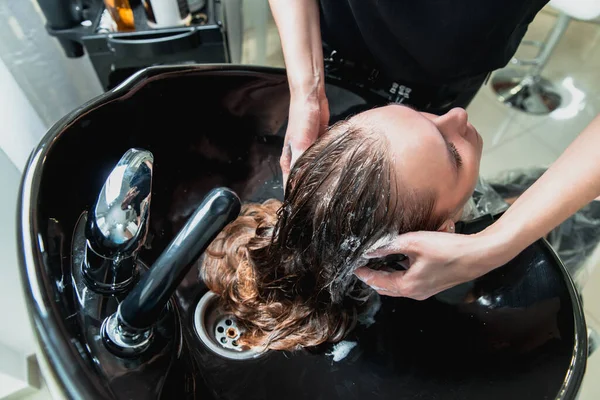 hair stylist washing hair of yong blonde girl in hair salon before haircut