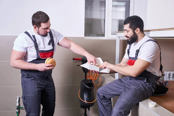 Two workers wearing uniform eating burger during lunch break — Stockfoto