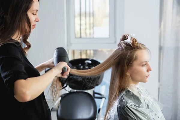 Крупный план рук парикмахеров, высушивающих длинные светлые волосы феном и круглой щеткой — стоковое фото