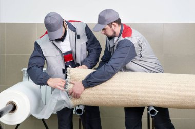 Men workers packing carpet in a plastic bag after cleaning it in automatic washing machine and dryer in the Laundry service