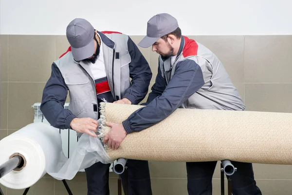 Men workers packing carpet in a plastic bag after cleaning it in automatic washing machine and dryer in the Laundry service — Stock Photo, Image