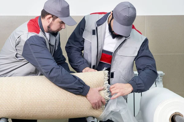 Los hombres trabajadores que embalan la alfombra en una bolsa de plástico después de limpiarla en lavadora automática y secadora en el servicio de lavandería —  Fotos de Stock