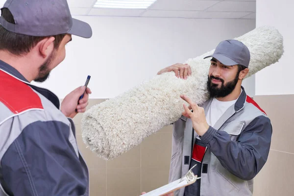 Dos hombres quitando una alfombra grande para el servicio de limpieza —  Fotos de Stock