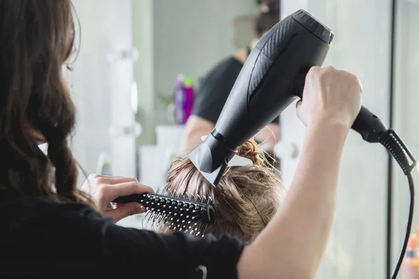 Close up of hairdressers hands drying long blond hair with blow dryer and round brush — Stock Photo, Image