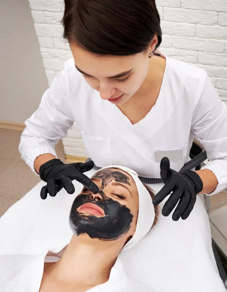 Косметолог наносить чорну маску на обличчя красивої жінки для вуглецевої шкірки — стокове фото