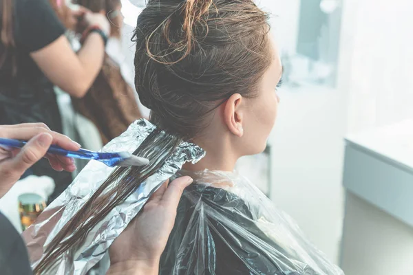 Hairdresser coloring young woman hair using foil
