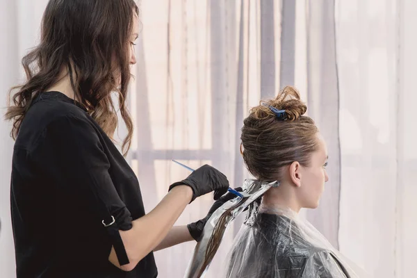 Hairdresser coloring young woman hair using foil — Stock Photo, Image