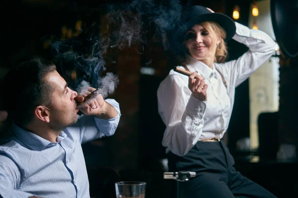 El hombre-gángster y la hermosa mujer mayor fumando cigarro en un bar —  Fotos de Stock