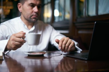 İş adamı laptopla çalışırken kafede kahve içiyor.
