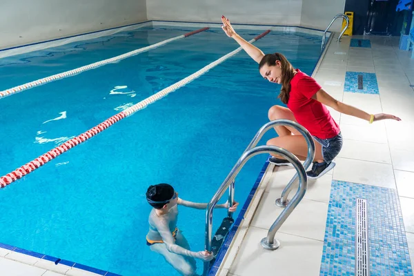 Entrenador femenino en el agua que da la lección de natación del niño preadolescente en la piscina cubierta —  Fotos de Stock