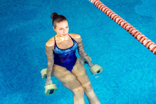 Jonge vrouw doet water aerobics in overdekt zwembad, sportief concept — Stockfoto