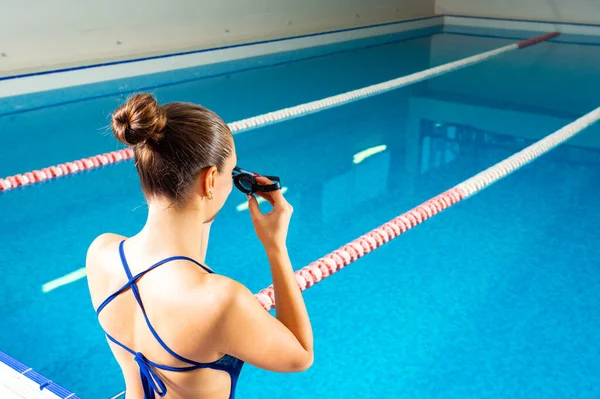Młoda kobieta w basenie trzyma gogle przygotowując się do pływania — Zdjęcie stockowe