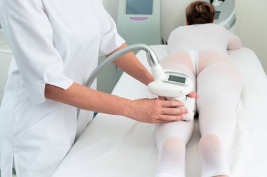 Beyaz takım elbiseli bir kadın spa salonunda selülit karşıtı masaj yaptırıyor. Klinikte LPG ve vücut şekillendirme tedavisi.