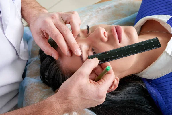 Schönheitschirurg und junge Frau mit Korrekturlinien vor Schönheitschirurgie, Zeichnung von Linien auf den Augen — Stockfoto