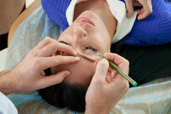 Cirurgião plástico e mulher jovem com linhas de correção antes da cirurgia estética, traçando linhas nos olhos — Fotografia de Stock