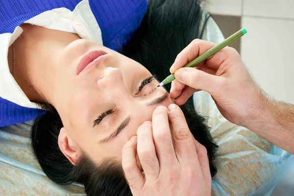 Cirurgião plástico e mulher jovem com linhas de correção antes da cirurgia estética, traçando linhas nos olhos — Fotografia de Stock