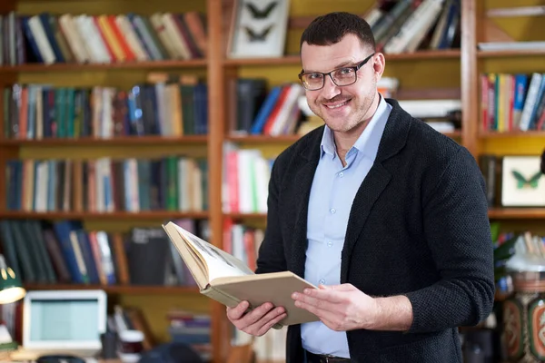 Hombre leyendo libro en la biblioteca de la universidad muchos libros en un fondo —  Fotos de Stock